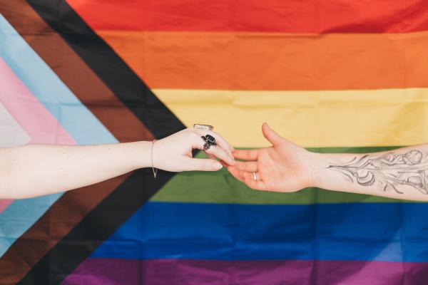 Zwei Personen reichen sich die Hand vor einer pride flag