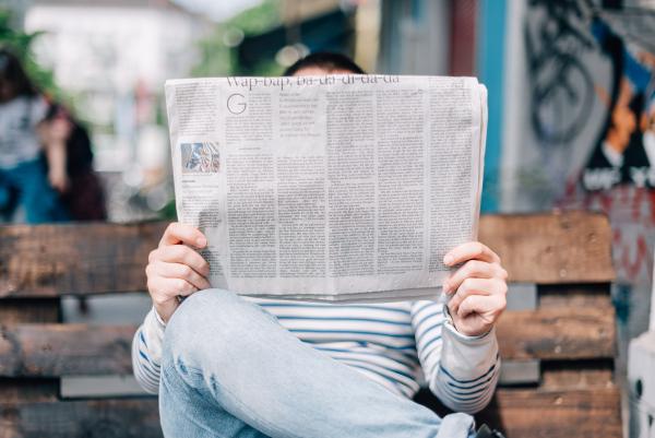 Mann sitzt auf einer Parkbank und liest eine Zeitung