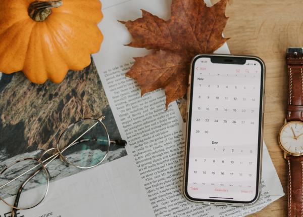 Zeitung auf Tisch mit Handy, Brille, Uhr, Kürbis und Herbstblatt