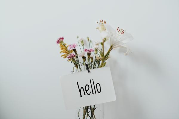 Vase mit Blumen und Zettel auf dem hello steht