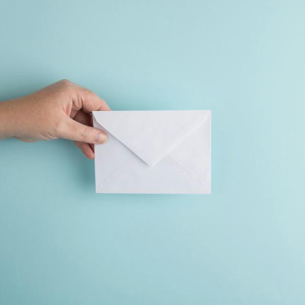 Hand mit einem offenen weißen Briefumschlag vor türkisem Hintergrund