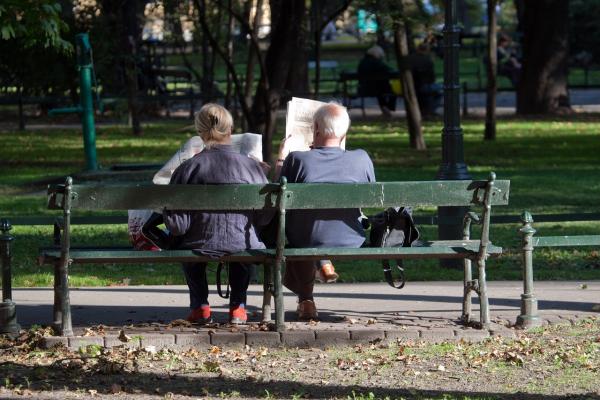 Zwei Personen sitzen Zeitung lesend auf einer Parkbank