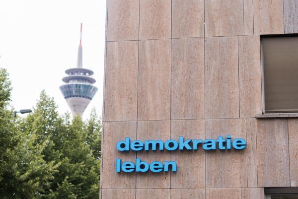 Schriftzug "Demokratie leben" auf Häuserfassade mit Rheinturm im Hintergrund