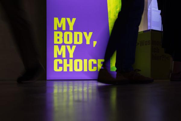 Foto einer Person, die an einem Schild vorbeigeht auf dem steht "My body, my choice"