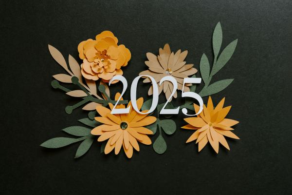 Zahl 2025 vor Papierblumen auf dunklem Hintergrund