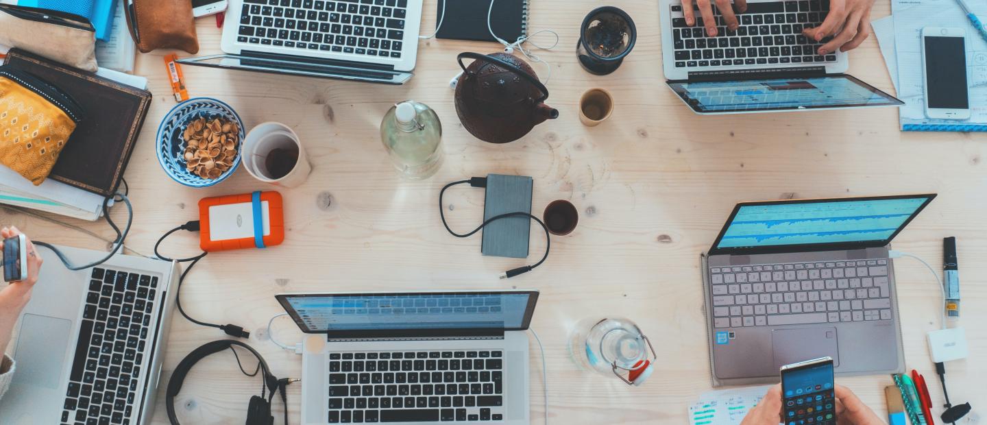 Tisch mit vielen Laptops und Arbeitsunterlagen